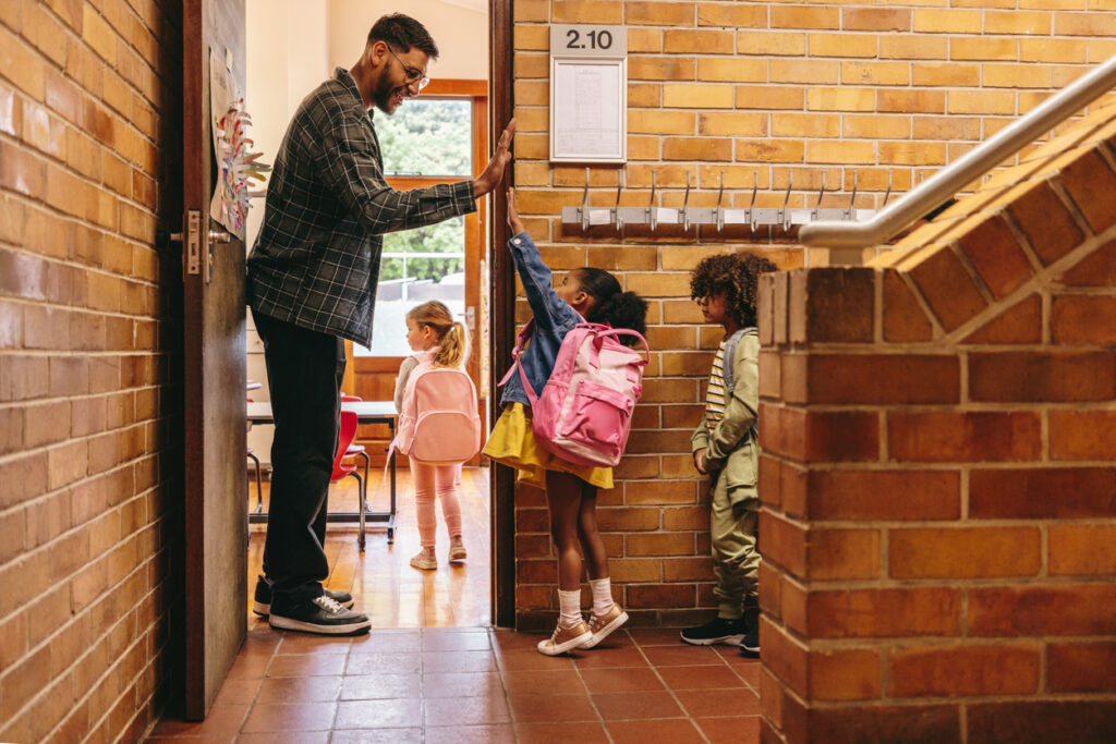 Elementary school teacher greeting his students at the door. Teacher welcoming his class with a high five.