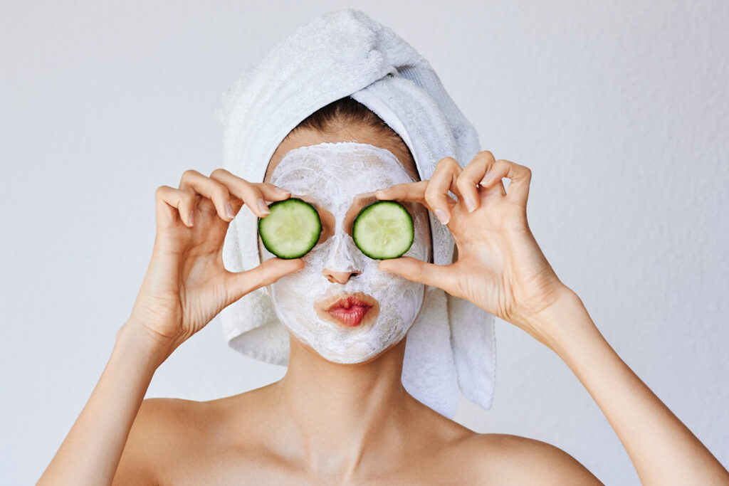 woman with facial mask and cucumbers over her eyes