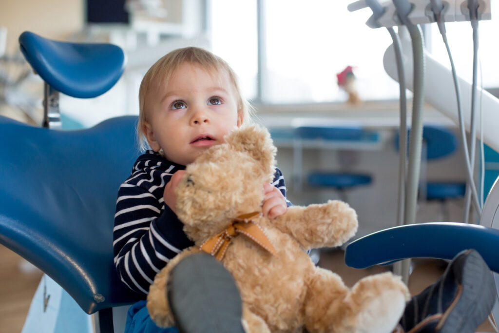 Little toddler boy with teddy bear toy at dentist's clinic for routine check-up, child alone sitting on dentist chair