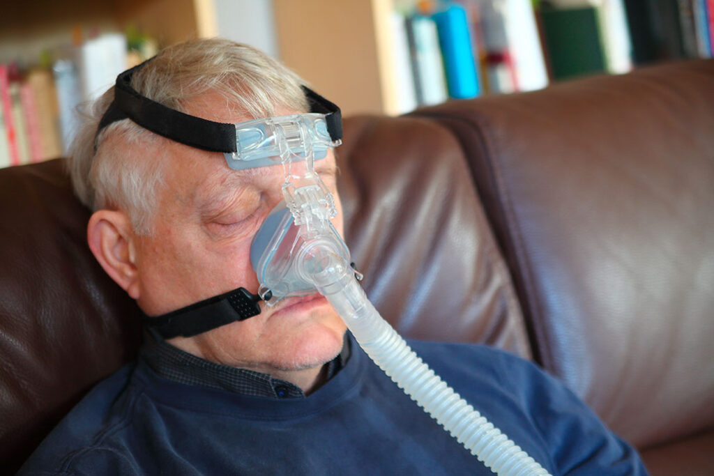 Senior man on sofa uses a breathing treatment machine