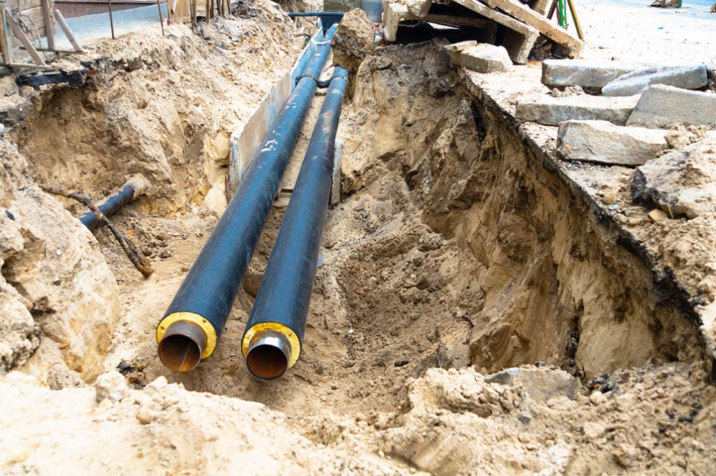 Two water pipes in ground pit trench ditch during plumbing under construction repairing.